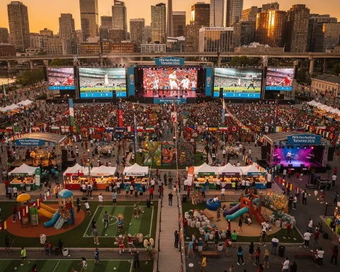 A lively outdoor FIFA Fan Festival event in Toronto, 2026, featuring large screens showing football matches, surrounded by a big crowd. The scene includes various tents, booths, a children's play area, a small sports area, and festive decorations with numerous flags. The Toronto city skyline with skyscrapers and the CN Tower is visible in the background.